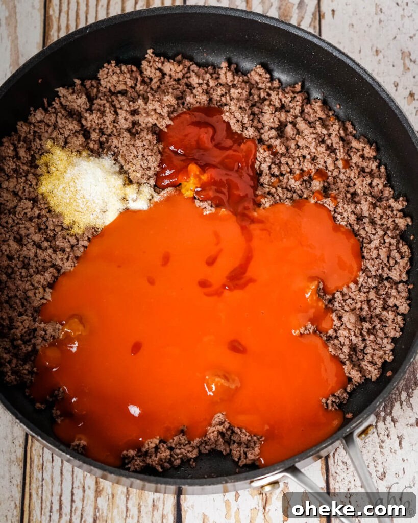 Garlic Bread Sloppy Joes: Cheesy Savory Sandwich Recipe 6 Tomato soup, Worcestershire sauce, yellow mustard, and ketchup, onion powder, salt, and garlic powder, and browned ground beef sitting in a medium black skillet.