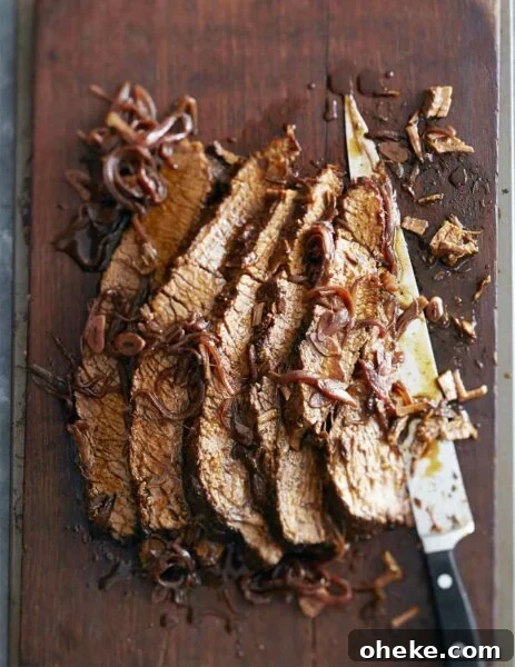 A sliced piece of braised brisket with red wine and honey laying on a cutting board with a large knife and covered with braised onions.