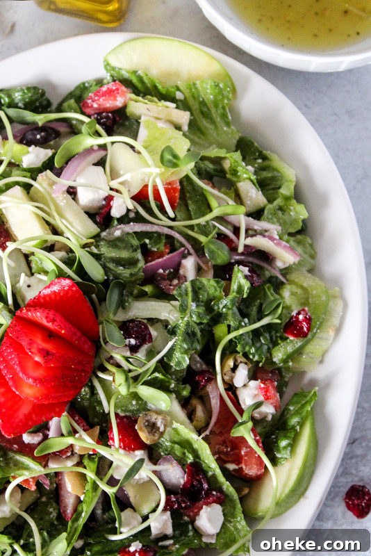 Cranberry and Feta Salad with Mixed Greens and Citrus Vinaigrette 2 A serving platter full of a colorful salad of romaine lettuce and vegetables with dressing and a strawberry on top