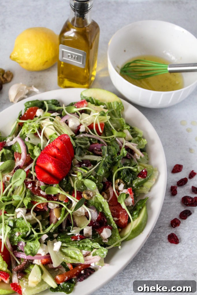 Cranberry and Feta Salad with Mixed Greens and Citrus Vinaigrette 5 A serving platter full of a colorful salad of romaine lettuce and vegetables with dressing and a strawberry on top and dried cranberries on the side of the platter