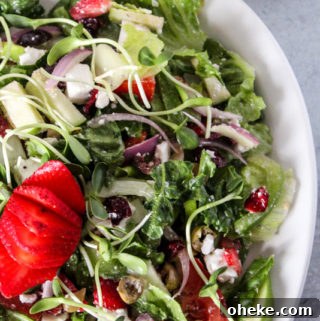 Cranberry and Feta Salad with Mixed Greens and Citrus Vinaigrette 6 A serving platter full of a colorful salad of romaine lettuce and vegetables with dressing and a strawberry on top