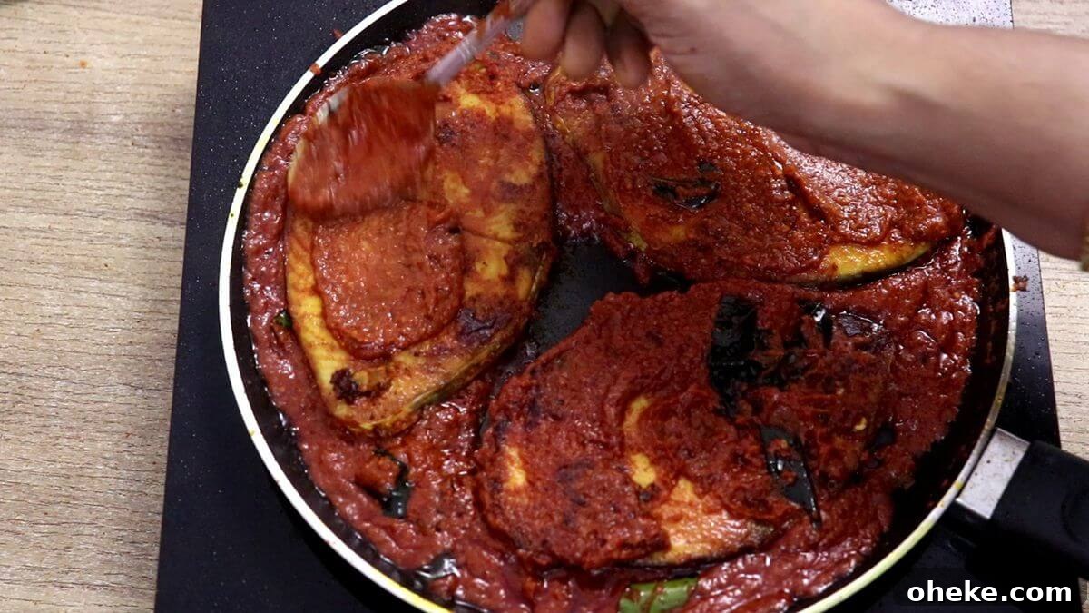 applying masala with a spoon on the fish for tawa fry recipe.
