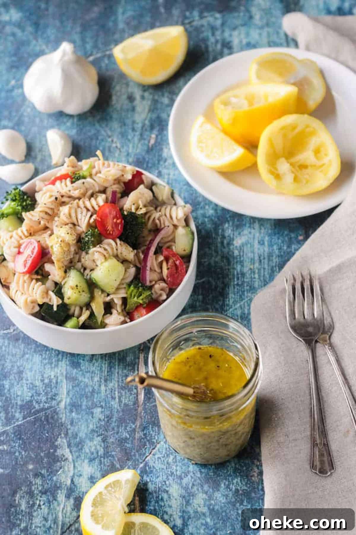 Zesty Lemon & Artichoke Pasta Salad Recipe for Summer 7 Small bowl of pasta salad next to a jar of vinaigrette and lemon slices.