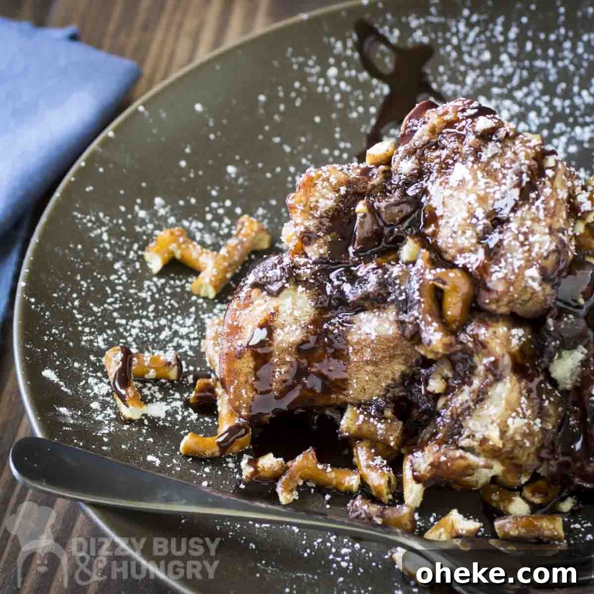 Chocolate Pretzel Biscuit Monkey Bread Recipe 11 Side shot of a slice of monkey bread sprinkled with powdered sugar on a grey plate with a fork on the side.