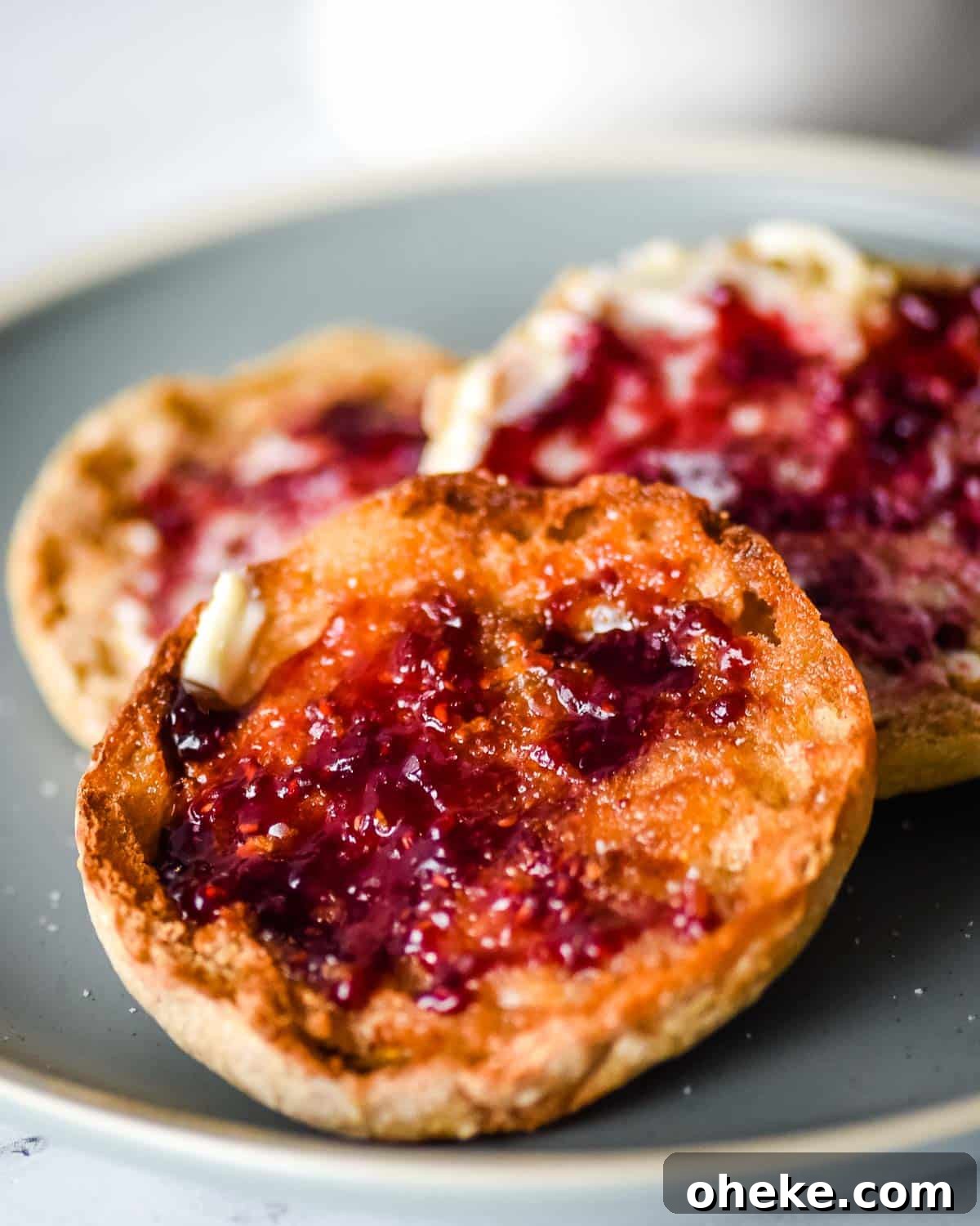 Three English muffins with butter and jam sit on a blue plate.