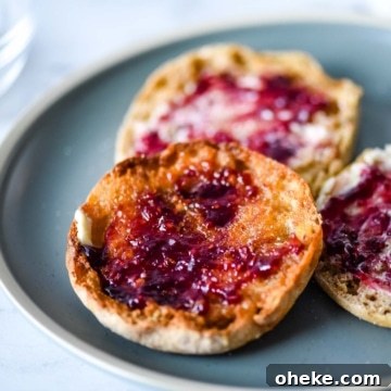 Three English muffins with butter and jam sit on a blue plate.
