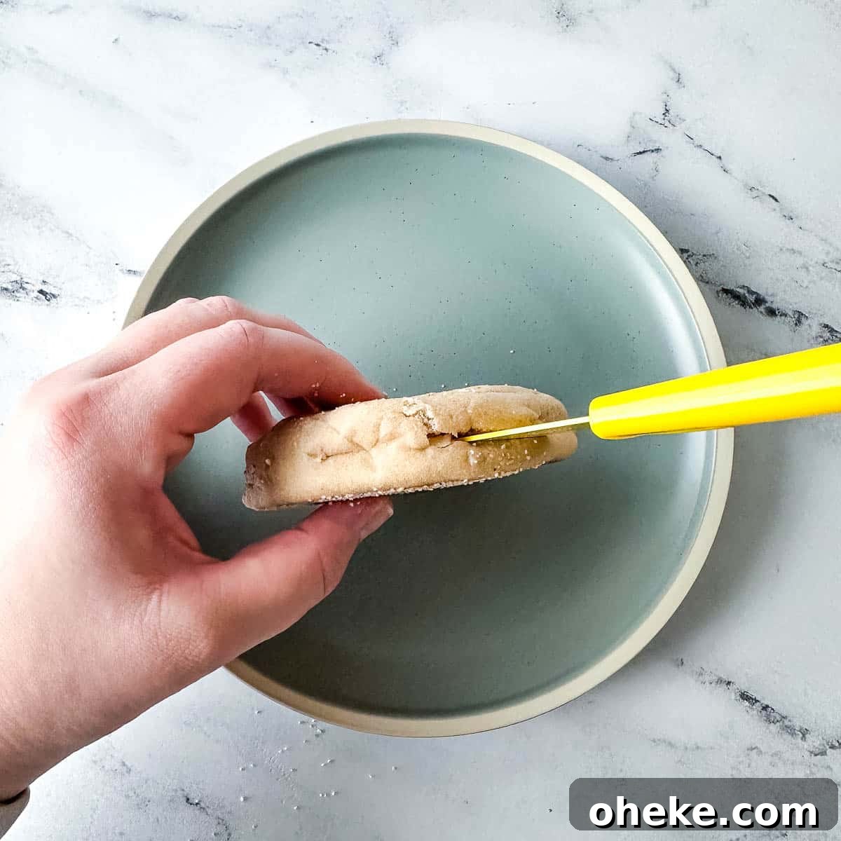 An English muffin is split with a yellow paring knife.