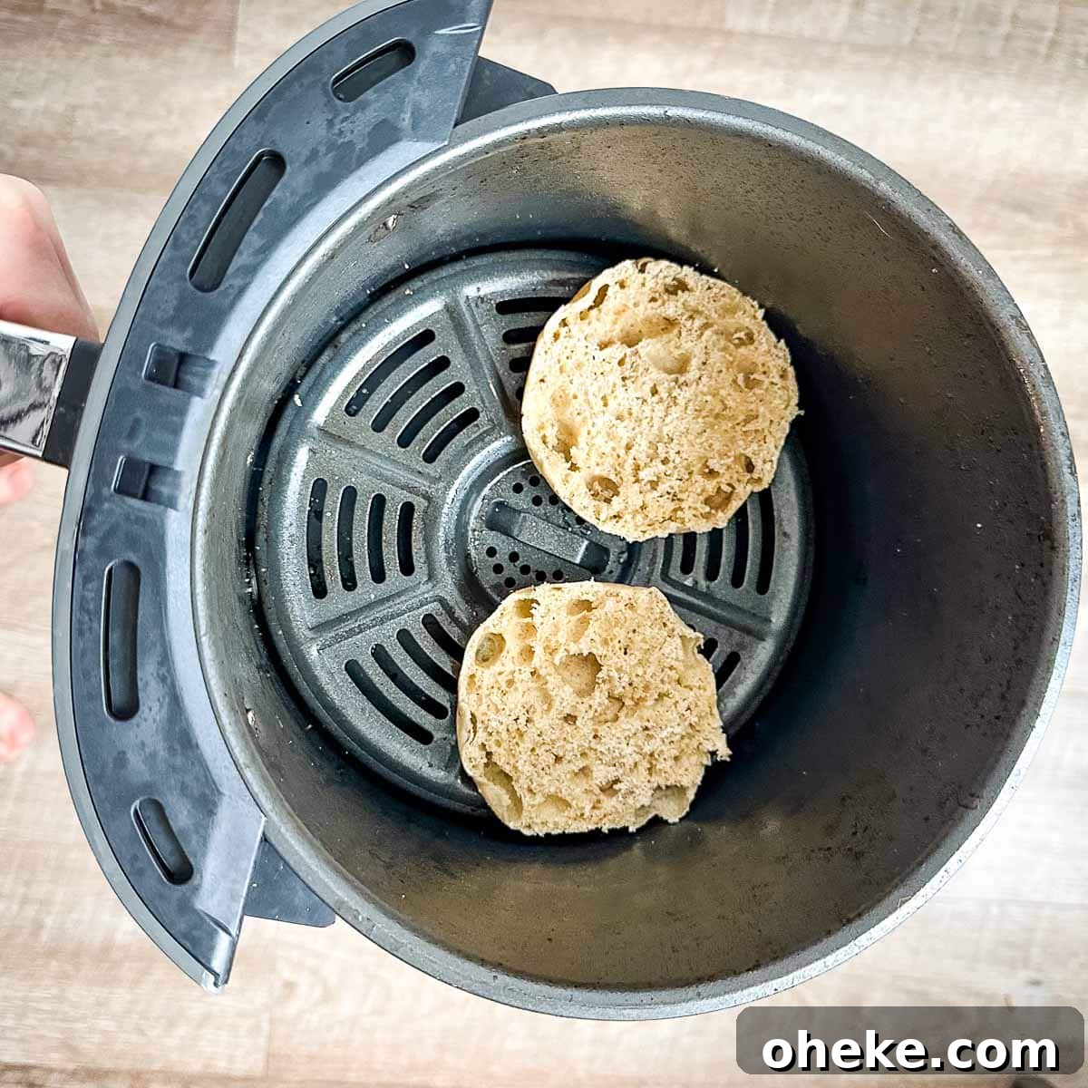 Halved English muffins sit in an air fryer basket.