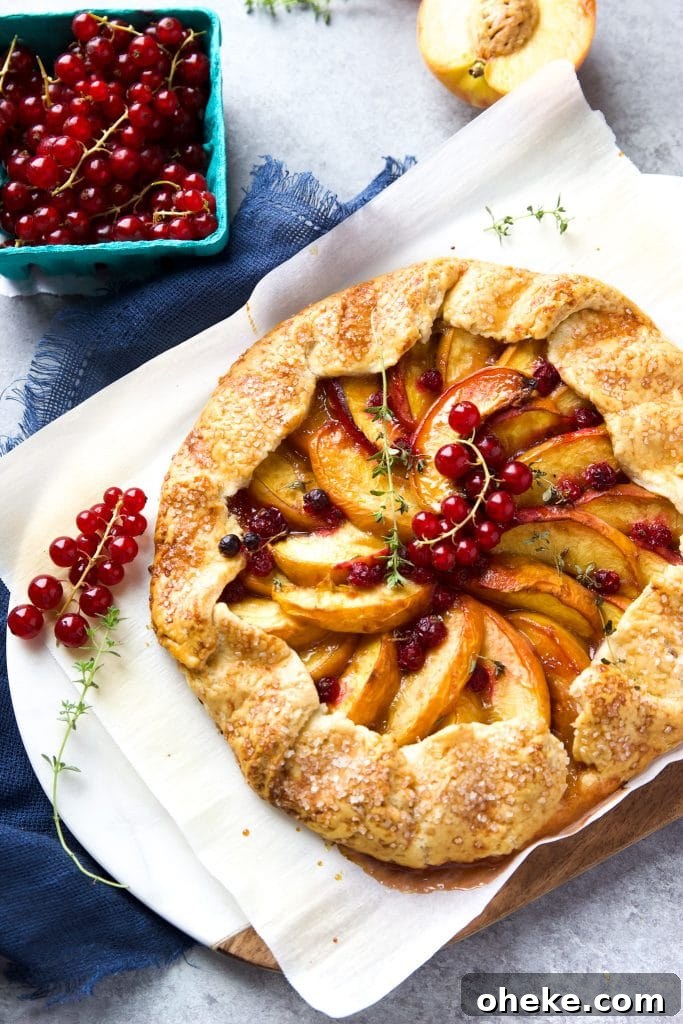 Perfect Peach Galette Recipe: Rustic Summer Tart with Almond Crust 2 Rustic peach galette with homemade buttery crust, juicy peaches and fresh currants, sitting on parchment paper
