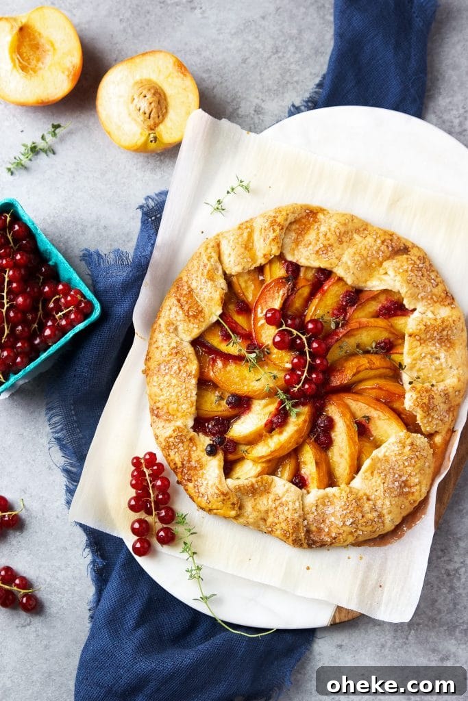 Perfect Peach Galette Recipe: Rustic Summer Tart with Almond Crust 3 Rustic peach galette with homemade buttery crust, juicy peaches and fresh currants, sitting on parchment paper