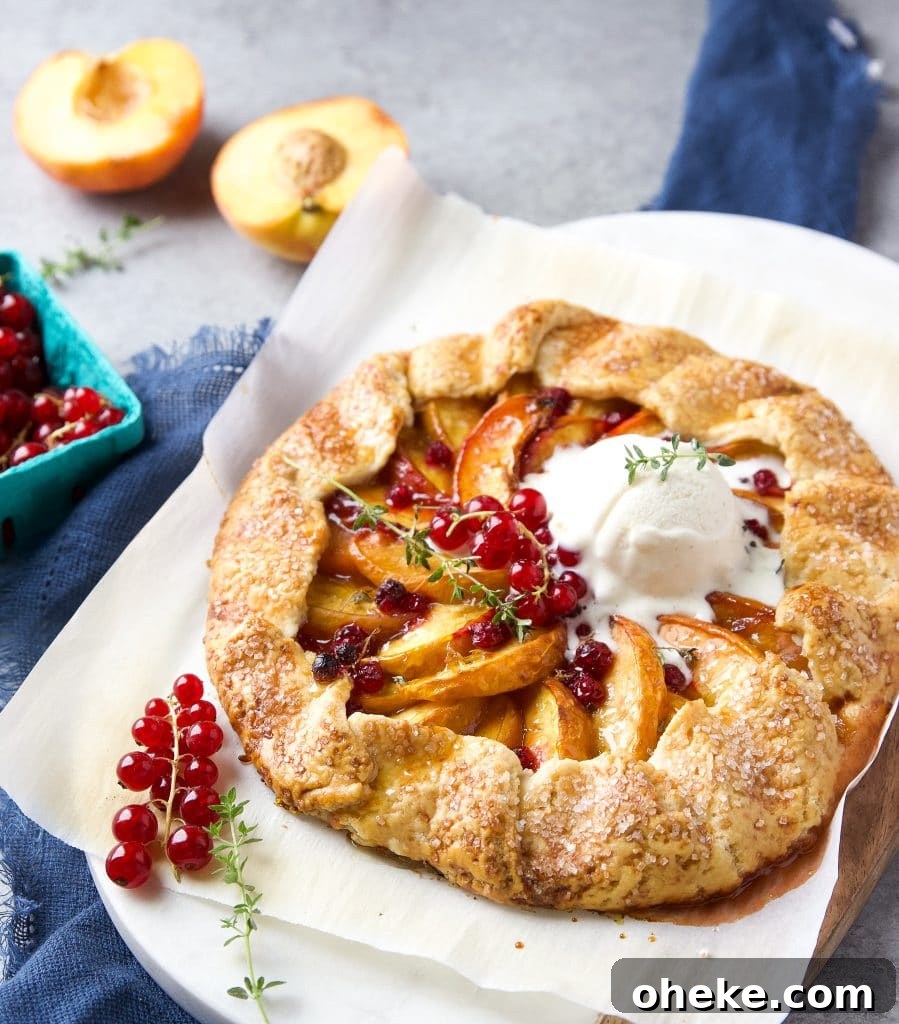 Perfect Peach Galette Recipe: Rustic Summer Tart with Almond Crust 4 Rustic peach galette with homemade buttery crust, juicy peaches and fresh currants, a scoop of vanilla ice cream, sitting on parchment paper