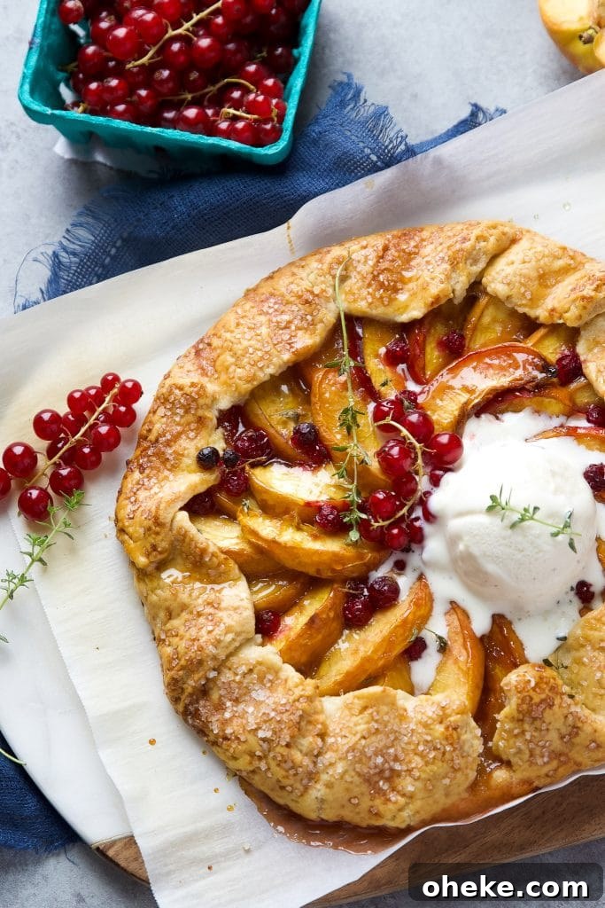 Perfect Peach Galette Recipe: Rustic Summer Tart with Almond Crust 5 Rustic peach galette with homemade buttery crust, juicy peaches, fresh currants and vanilla ice cream, sitting on parchment paper