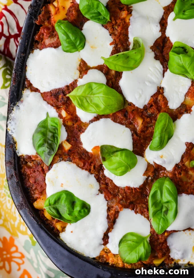 Slow-Cooker Lasagna Recipe for Tender, Cheesy Layers 2 A cooked crockpot lasagna with dollops of fresh mozzarella cheese and fresh basil leaves. A colorful napkin sits beside the crockpot.
