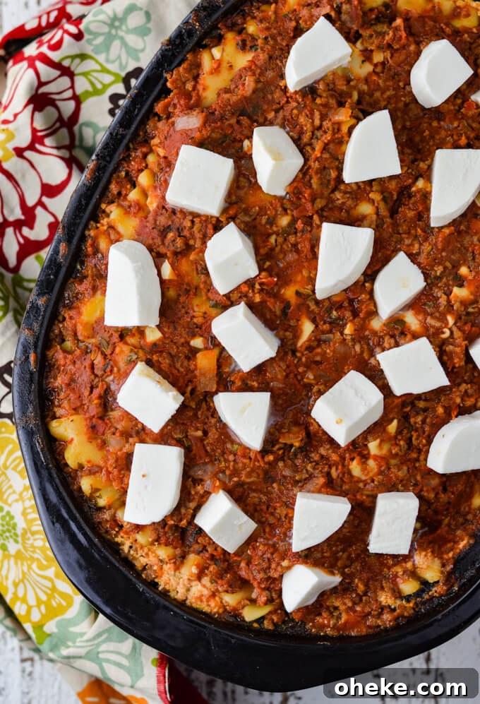 Slow-Cooker Lasagna Recipe for Tender, Cheesy Layers 11 A crockpot of cooked lasagna with cubes of uncooked fresh mozzarella cheese. A colorful napkin sits next to the pot.