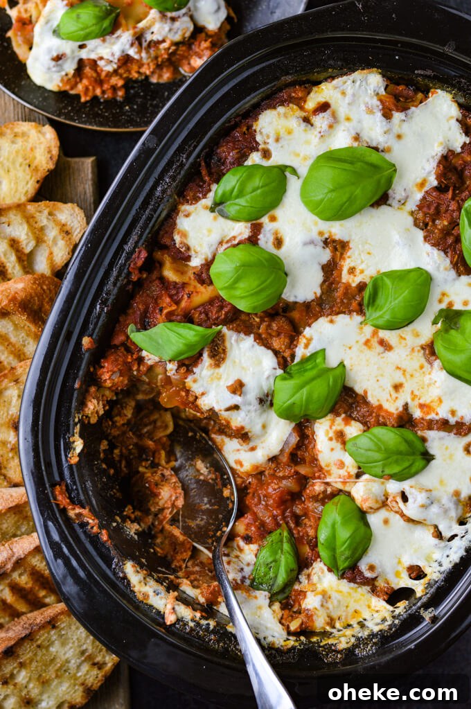 Slow-Cooker Lasagna Recipe for Tender, Cheesy Layers 12 A cooked crockpot lasagna with dollops of fresh mozzarella cheese and fresh basil leaves. A spoonful has been removed from the pan.
