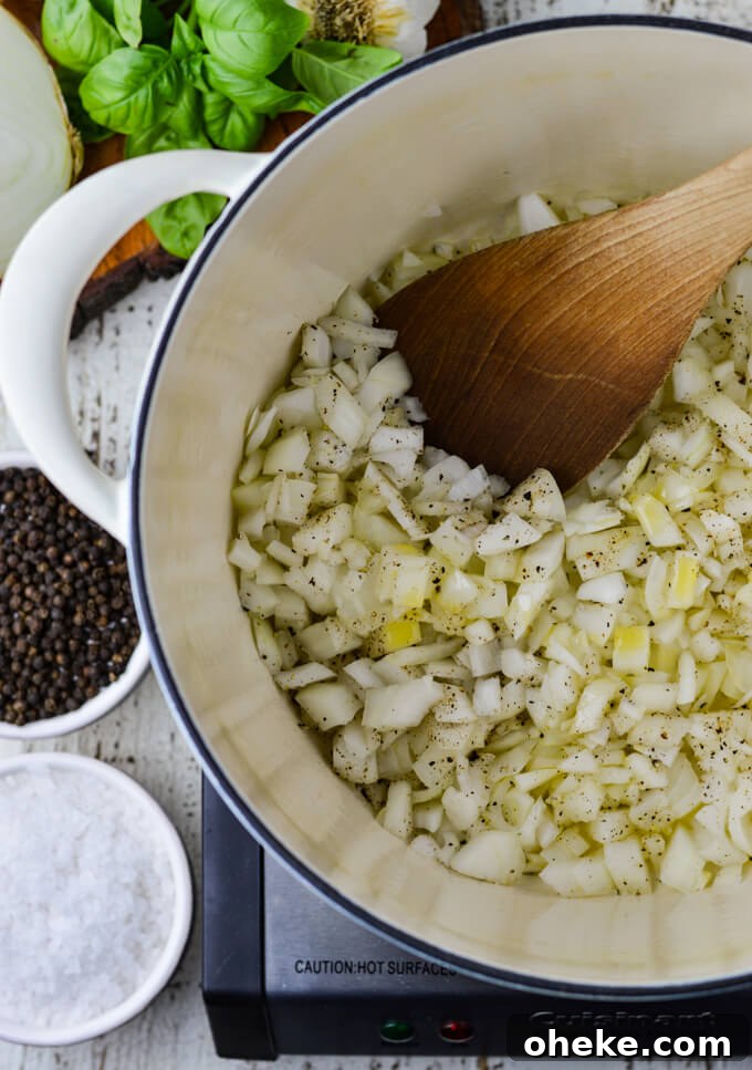 Slow-Cooker Lasagna Recipe for Tender, Cheesy Layers 3 Sauteed onions in a white dutch oven with a wooden spoon stirring the onions. Black Peppercorns and coarse sea salt in small white bowls, fresh basil, garlic bulb and ½ onion sits next to the pan.