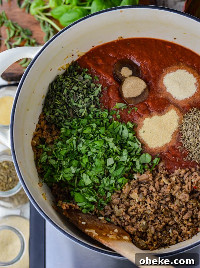 Slow-Cooker Lasagna Recipe for Tender, Cheesy Layers 6 Crushed tomatoes, cooked chorizo, fresh oregano, fresh basil, and spices sit in a white Dutch oven. Jars spices and fresh herbs sit beside the pan.