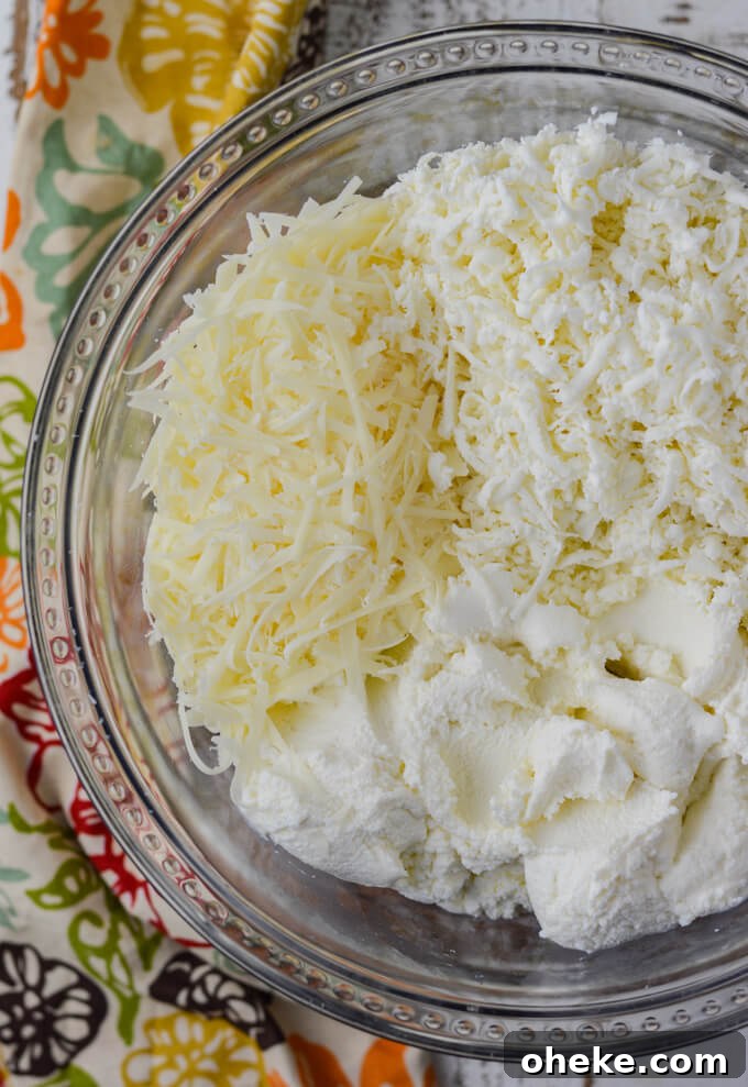 Slow-Cooker Lasagna Recipe for Tender, Cheesy Layers 8 Grated parmesan, fresh mozzarello and ricotta cheese sit in a clear glass bowl with a colorful napkin sitting beside it.