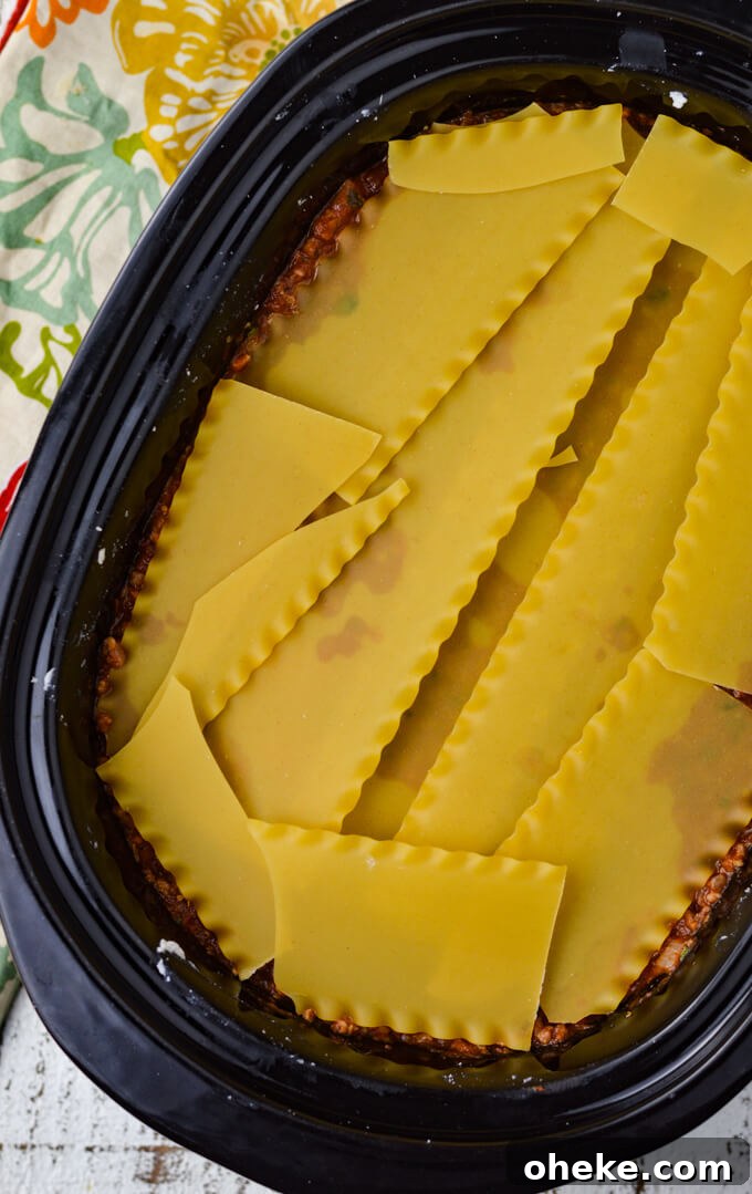 Slow-Cooker Lasagna Recipe for Tender, Cheesy Layers 9 A crockpot holds layers of lasagna with a shot of dry noodles broken to fit in the pan.
