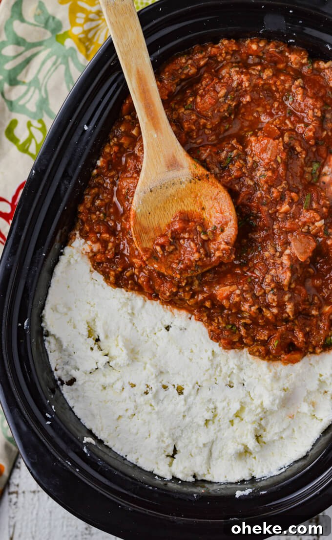 Slow-Cooker Lasagna Recipe for Tender, Cheesy Layers 10 A photo showing how to layer lasagna in a crockpot. Half spaghetti sauce and half cheese mixture with a wooden spoon sitting on them.