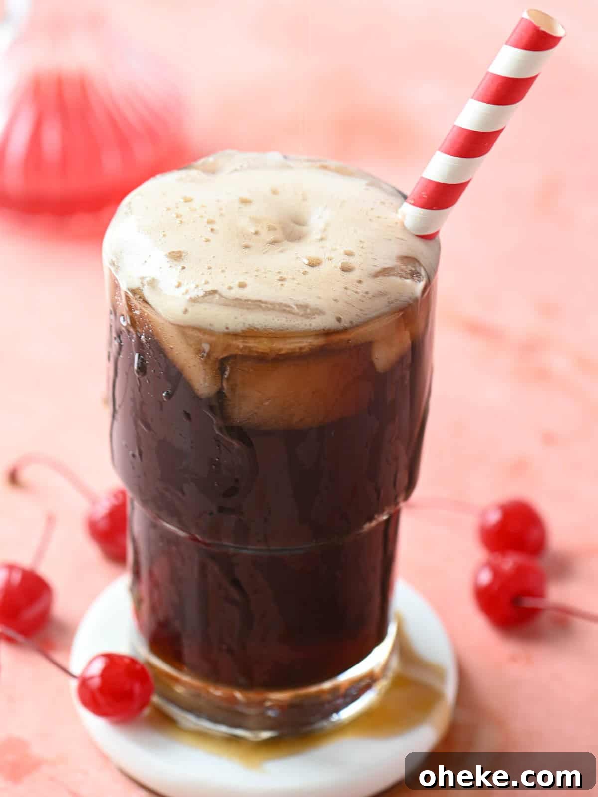 Cherry Americola: Refreshing Cherry-Flavored Coffee Drink 5 A cherry americola drink in a clear glass with a straw on a pink surface.