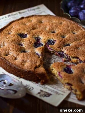 Angled view of plum cake with a slice removed on a wood surface.