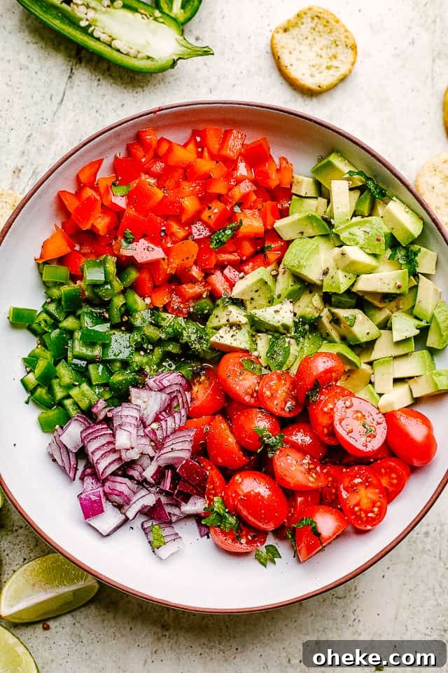 This avocado salsa is a next-level Cinco de Mayo recipe! It's creamy, chunky, and 100% addictive. It's like a flavor party in one bowl! diced peppers, jalapenos, tomatoes, avocado, and red onions in a salad bowl