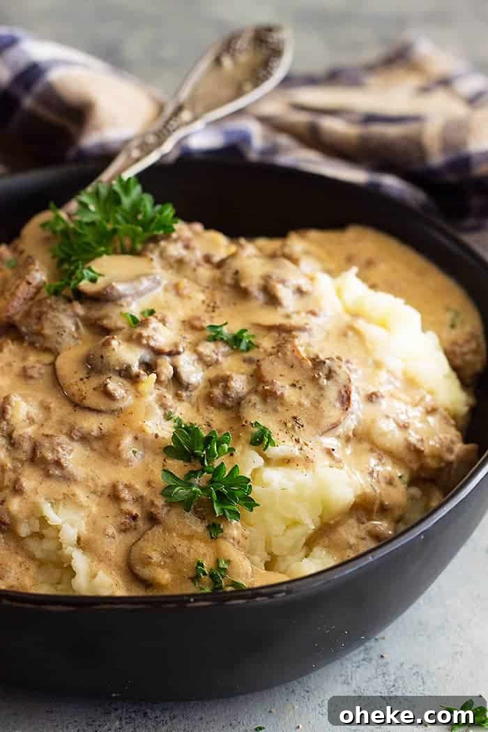 Creamy Ground Beef Stroganoff Recipe for Weeknight Dinners 5 closeup: saucy hamburger beef stroganoff recipe over mashed potatoes with fresh herbs on top