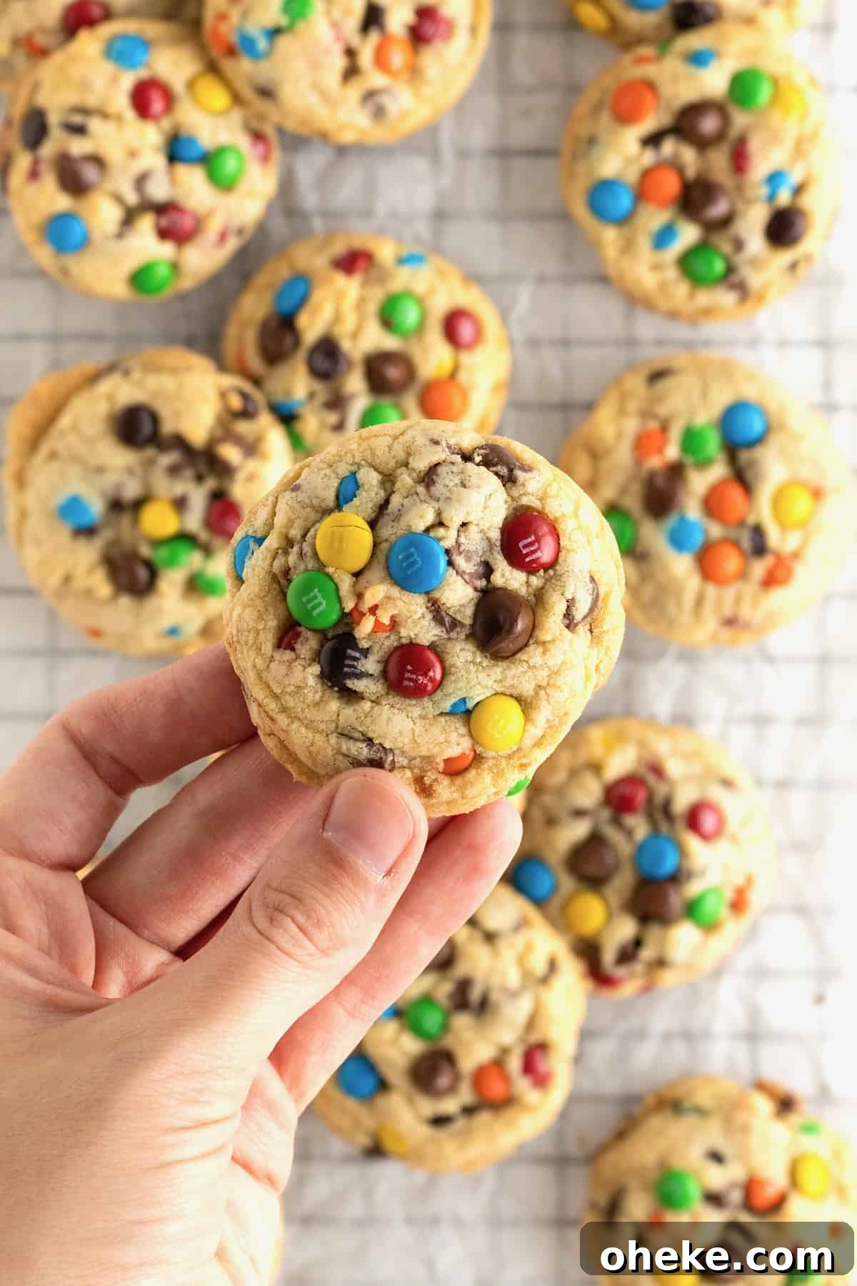 A hand holding a cookie with cookies with M&Ms and chocolate chips in it.