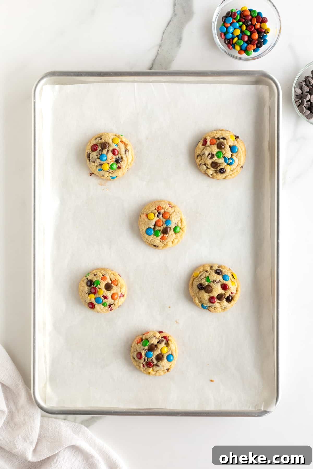 Baked M&M chocolate chip cookies on a parchment lined baking sheet.