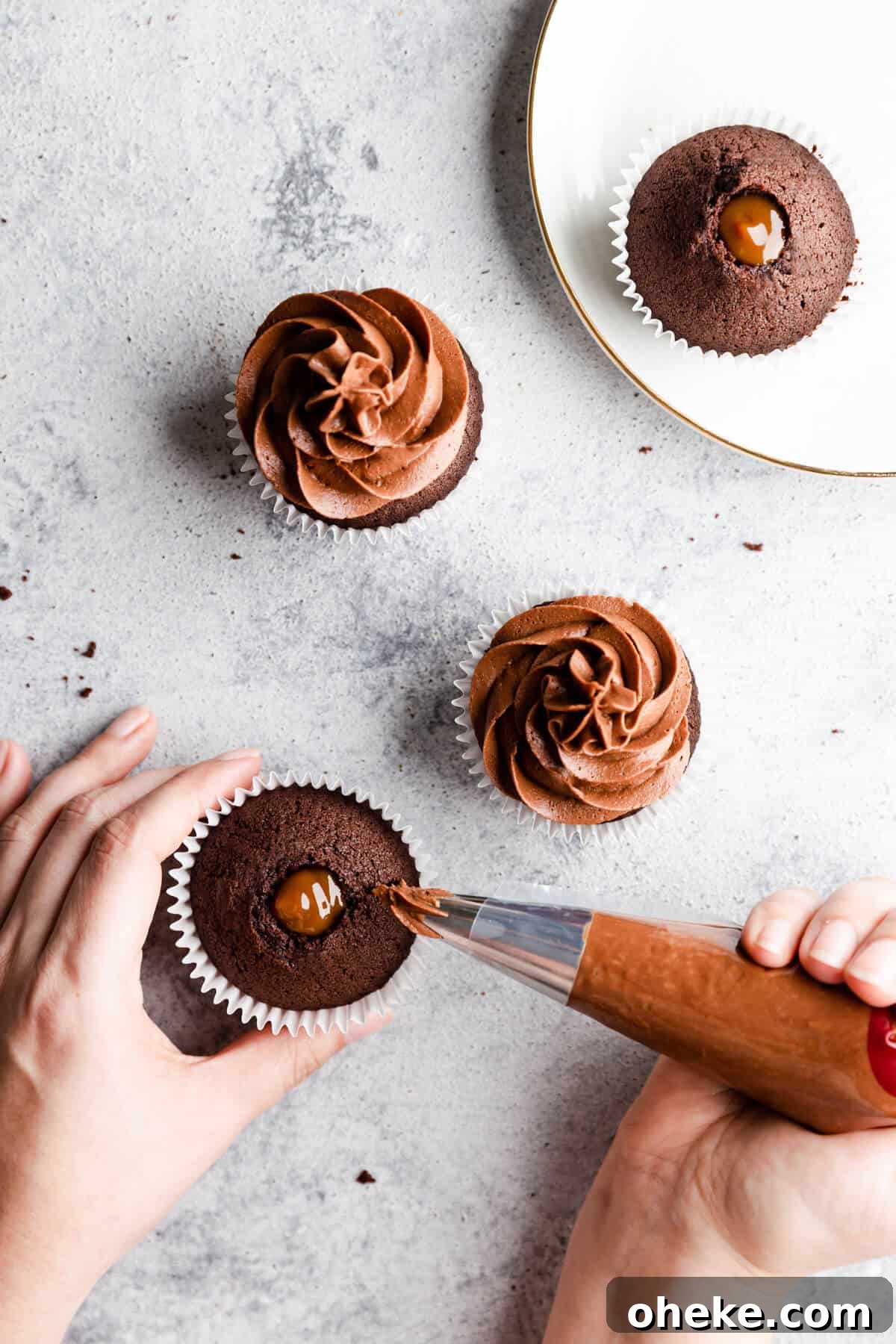 top view of chocolate cupcakes being topped with chocolate buttercream