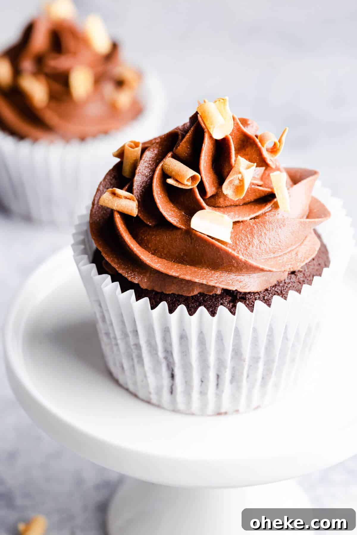 a side angle photo of a single chocolate cupcake on a small white cupcake stand