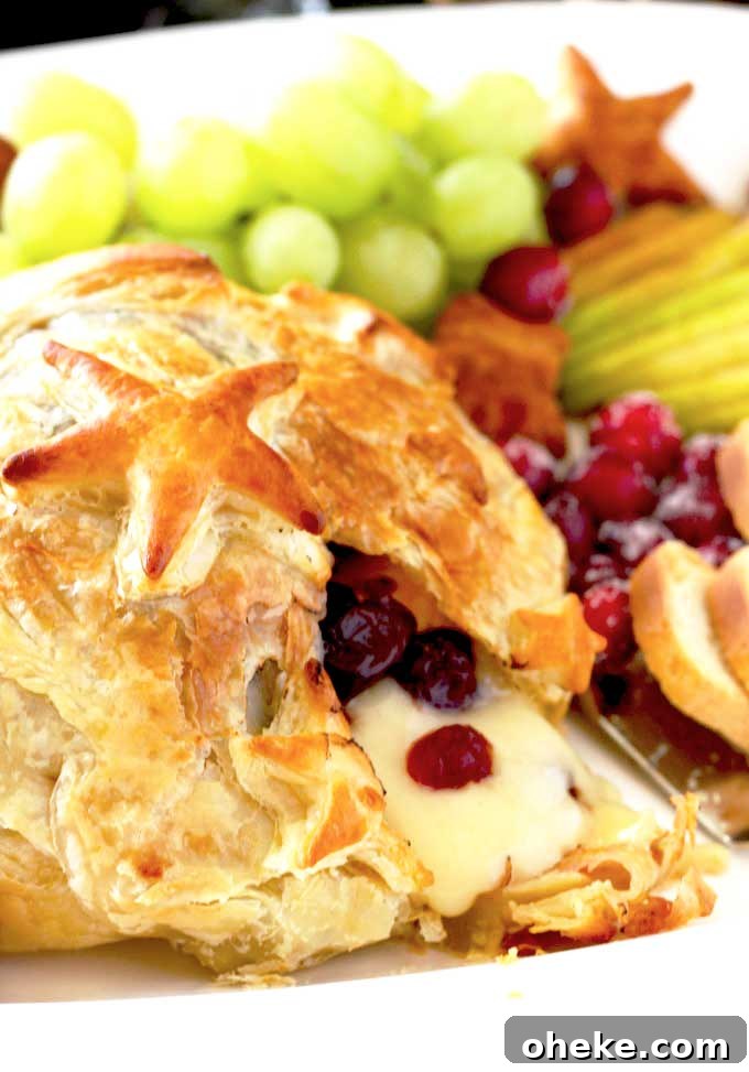 Baked Brie en Croûte with Cranberries and Puff Pastry 2 Close up of melted baked Brie served with fruit and crackers