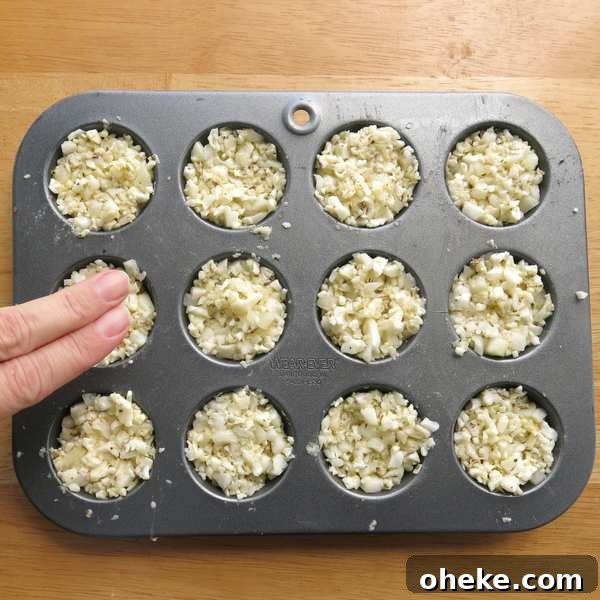 Two fingers pressing down on cauliflower egg muffins to compact the mixture