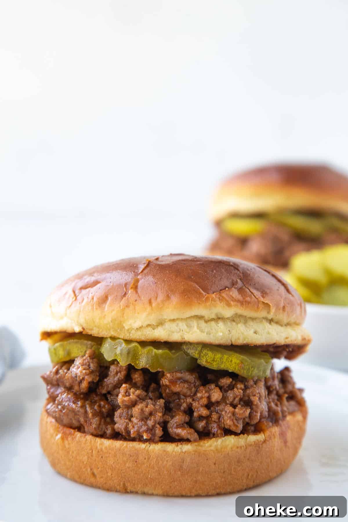 old fashioned sloppy joe sandwich on brioche with pickle chips, sitting on a white plate.