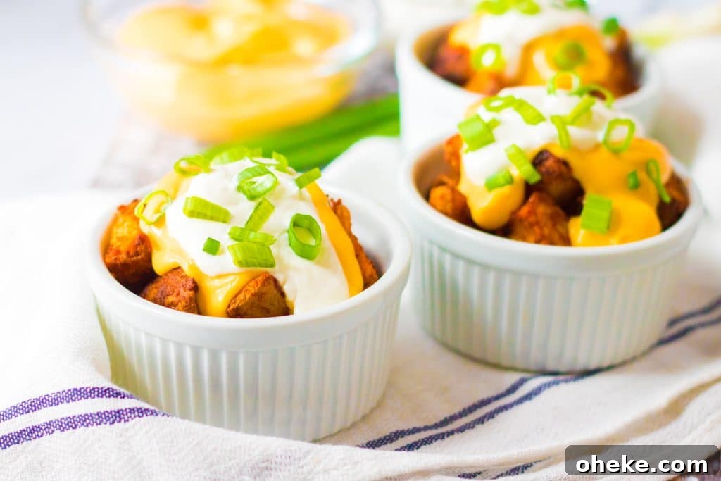Air Fryer Cheesy Fiesta Potatoes — Taco Bell Copycat Recipe 3 cheesy fiesta potatoes topped with sour cream and sliced green onions in small white ramekins