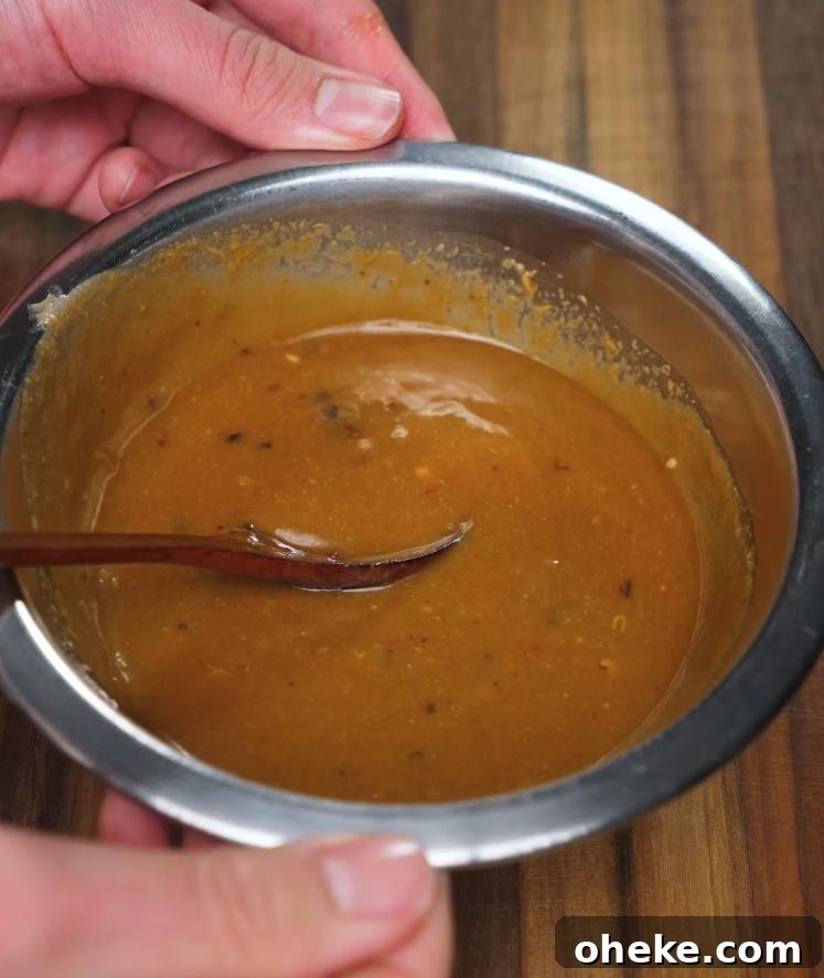 Spicy Peanut Noodles with Garlic and Chili Oil 4 The completed spicy peanut butter sauce is shown in a metal mixing bowl, smooth and thick with a spoon resting inside, ready to be poured over the noodles.