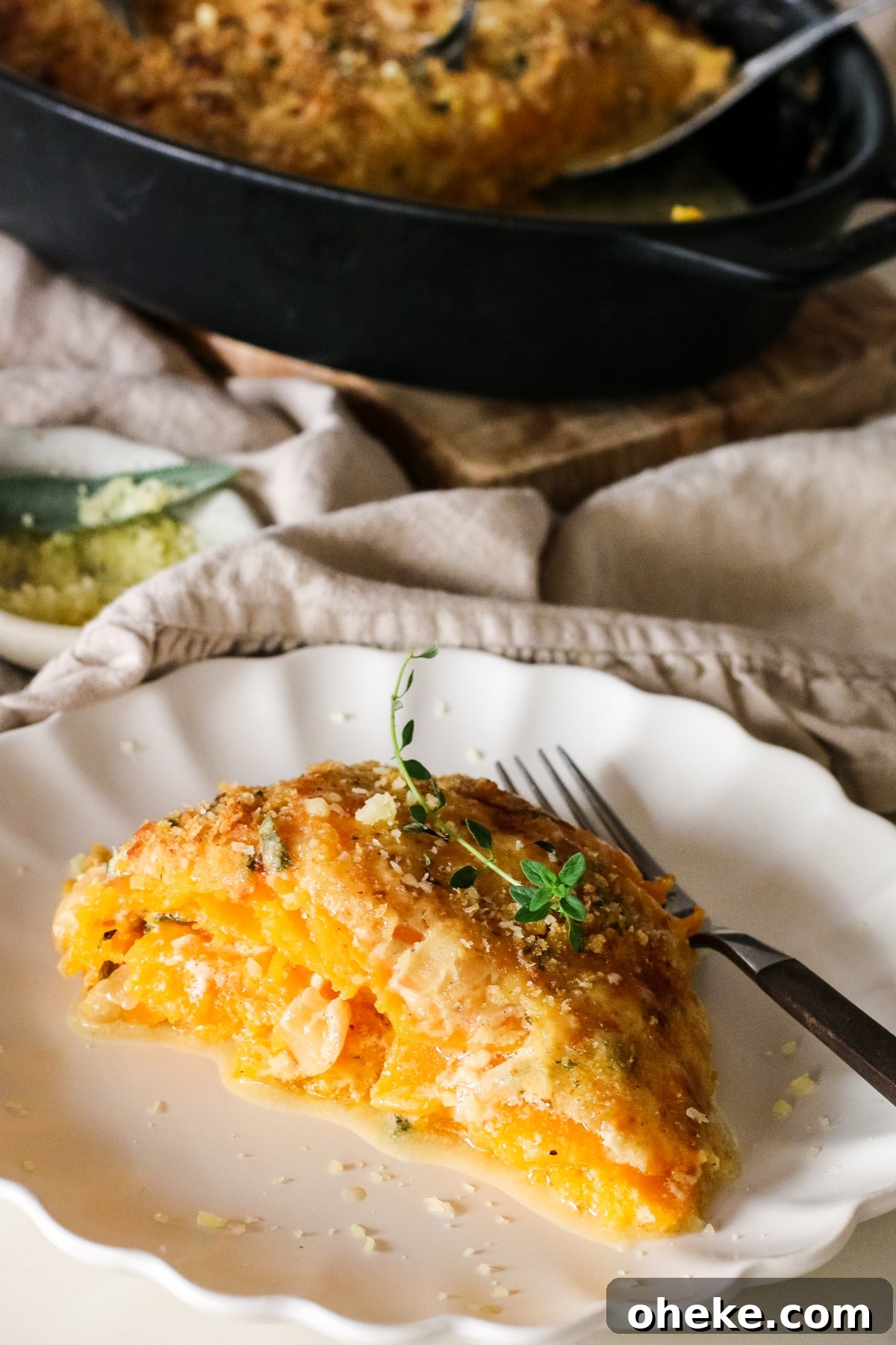 butternut squash gratin slice on a plate with a fork infront of baking dish.