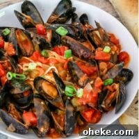 A bowl of mussels with Creole sauce, linguine, and a baguette on the side.