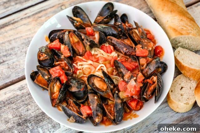 Creole style mussels with tomatoes and linguine in a wide shallow bowl.