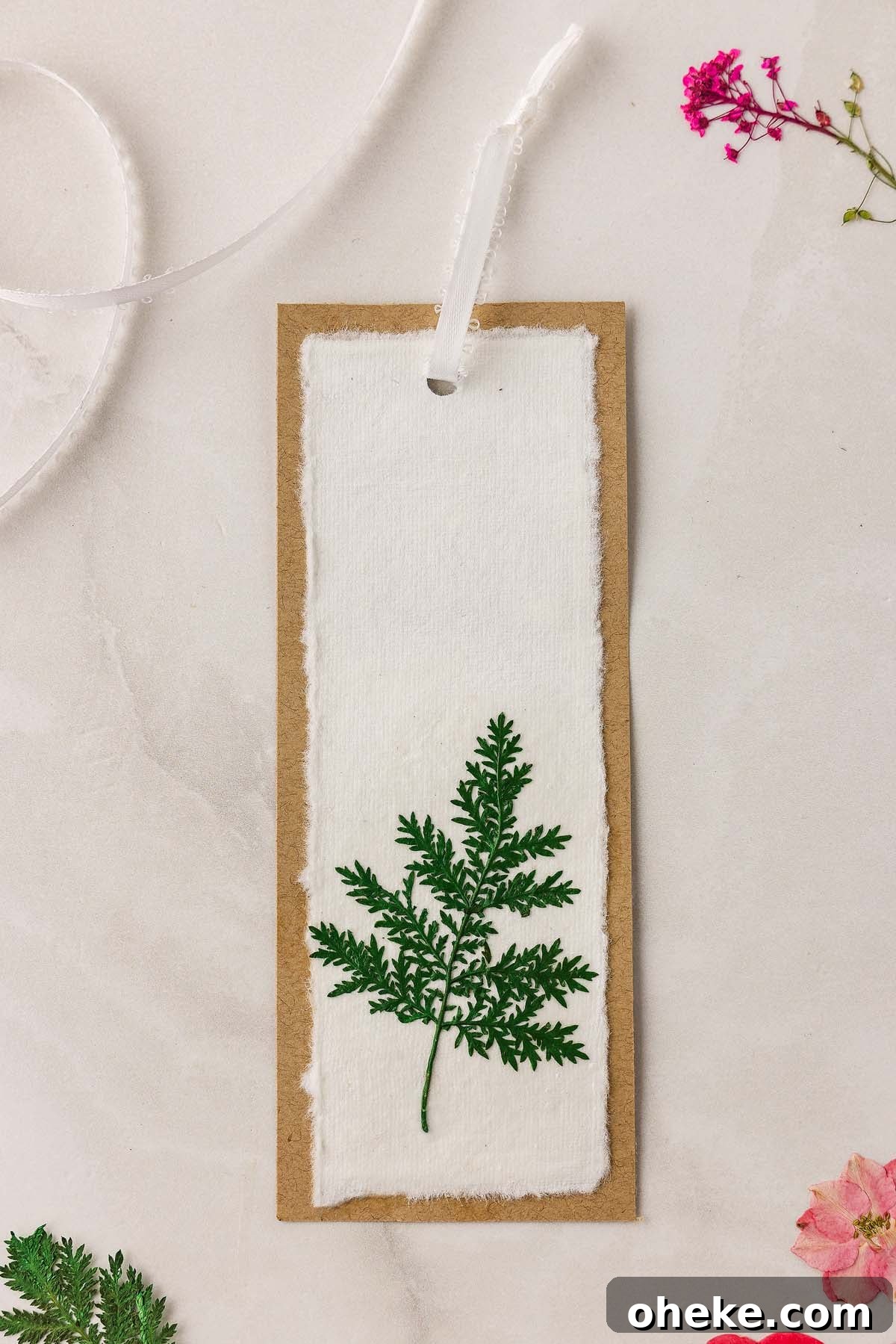 DIY Pressed Flower Bookmarks: Step-by-Step Craft Tutorial 19 A handmade pressed flower bookmark DIY featuring a real green fern leaf on white fabric, finished with a delicate white ribbon.