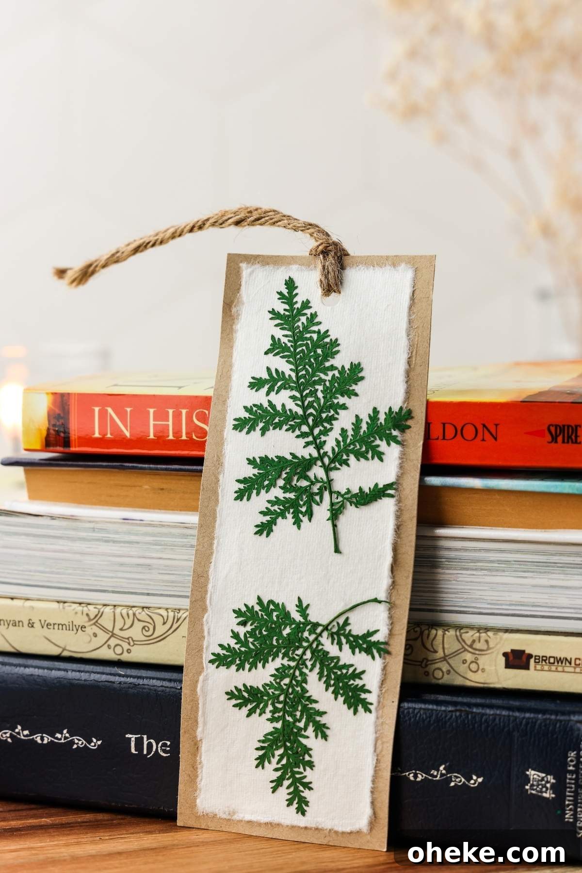 DIY Pressed Flower Bookmarks: Step-by-Step Craft Tutorial 7 A handmade DIY bookmark with pressed green ferns and a twine tassel rests on a stack of books.