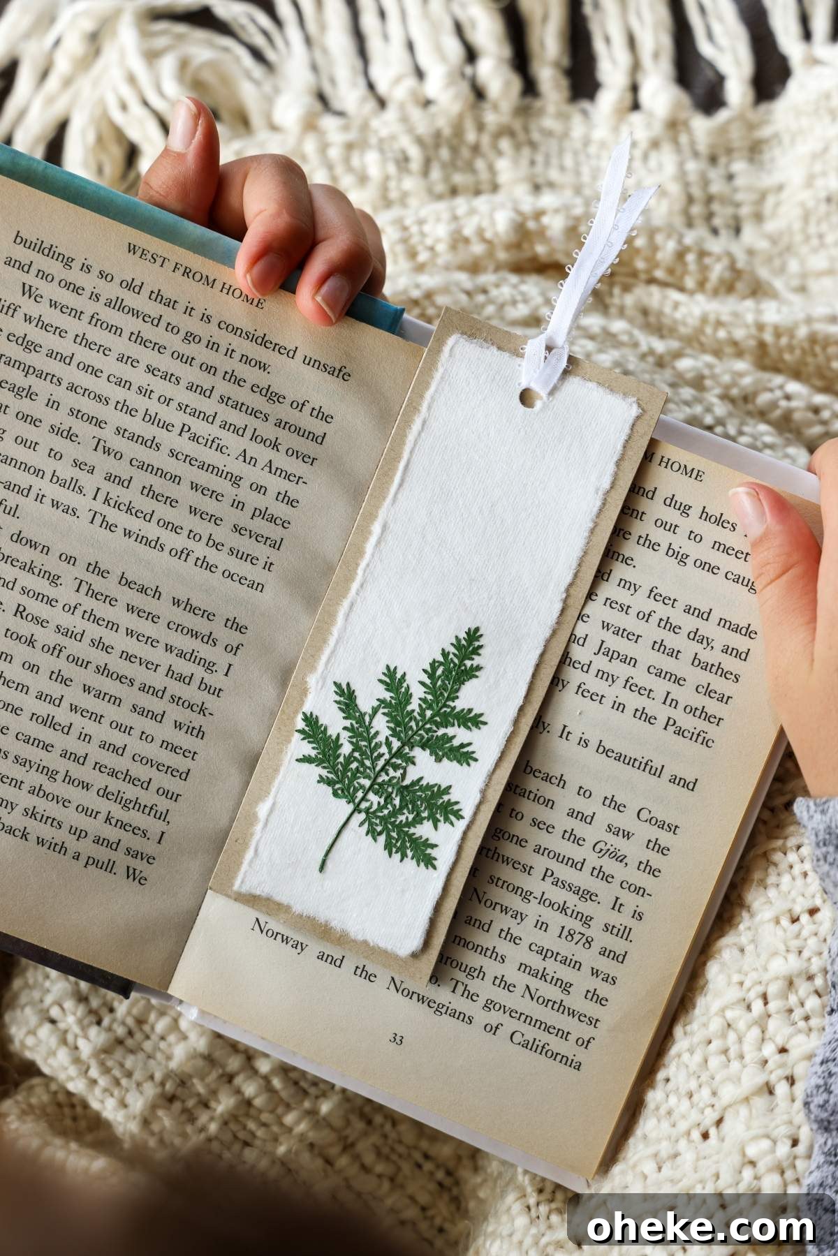 DIY Pressed Flower Bookmarks: Step-by-Step Craft Tutorial 8 A person holds an open book adorned with a DIY bookmark, elegantly crafted from pressed flowers and ferns.
