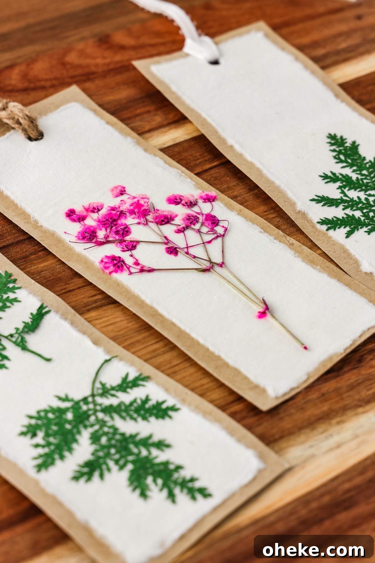 DIY Pressed Flower Bookmarks: Step-by-Step Craft Tutorial 9 Three handmade pressed flower bookmarks with vibrant pink flowers and lush green leaves elegantly displayed on a rustic wooden surface, showcasing the art of DIY craftsmanship.