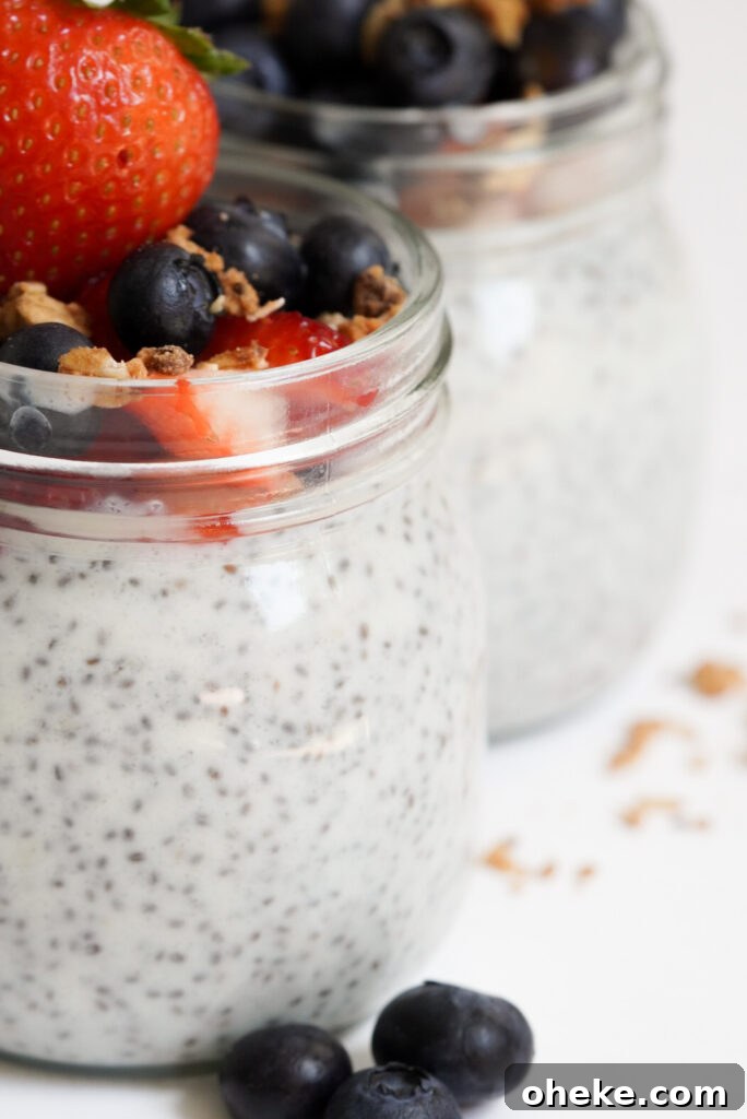 High-Protein Chia Pudding Recipe for Muscle Fuel 8 closeup shot of two rounded mason jras filled with high protein chia seed pudding topped with berries and granola.