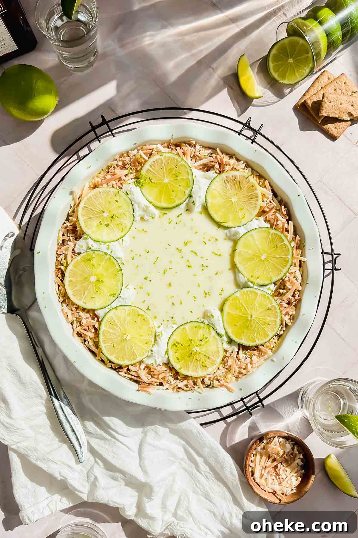 Tequila Lime Key Lime Pie Recipe with a Boozy Graham Cracker Crust 2 tequila key lime pie garnished with toasted coconut and lime slices in white baking dish.
