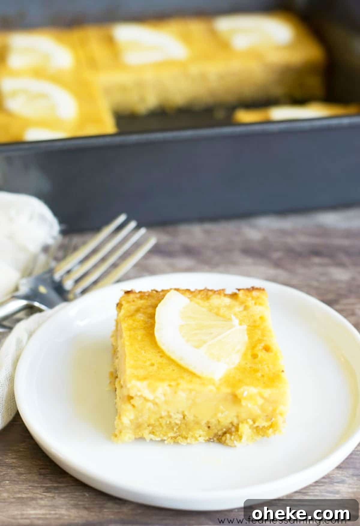 Paleo Lemon Bars with Almond-Coconut Crust Recipe 2 A paleo lemon bar on a small white plate in front of the pan.