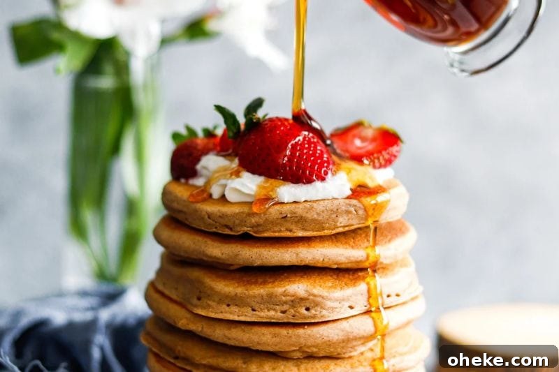A close up of maple syrup being poured on a stack of buttermilk pancakes.