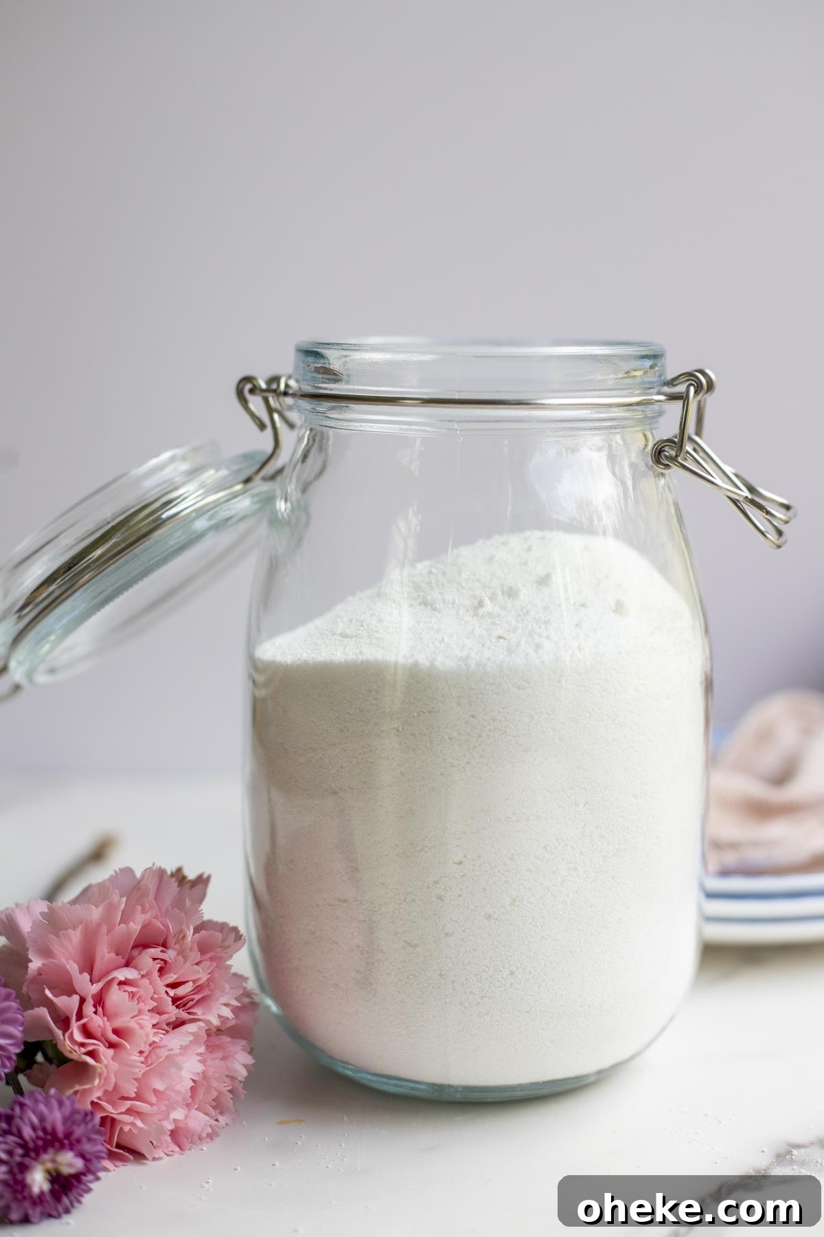 Homemade dishwasher detergent in a swing top jar on a countertop surrounded by flowers.