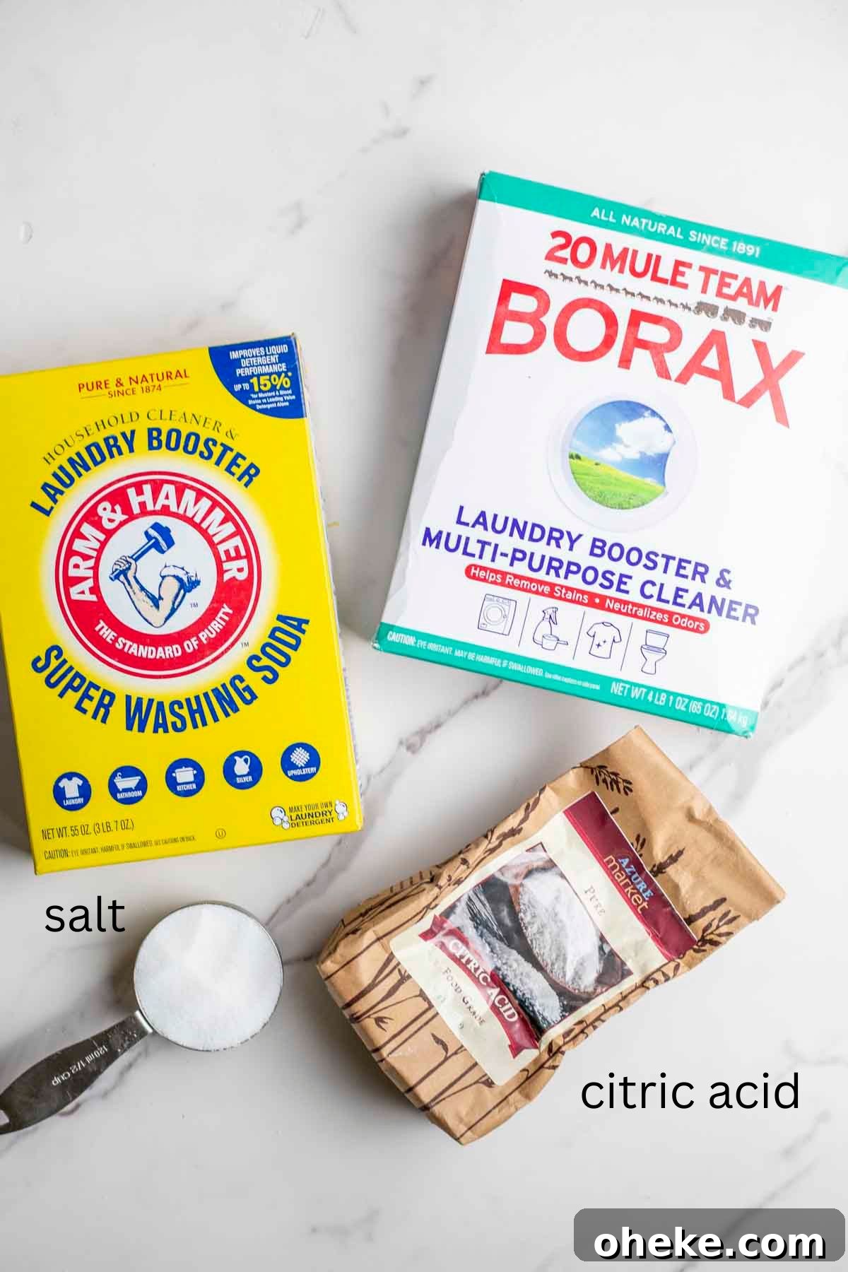 A box of Borax, washing soda, citric acid and a measuring cup of salt on a marble countertop.